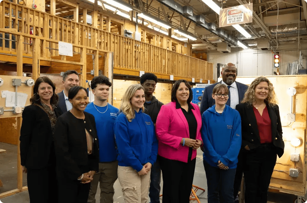 A group of people stands together in an educational workspace, surrounded by wooden structures and various electrical equipment.