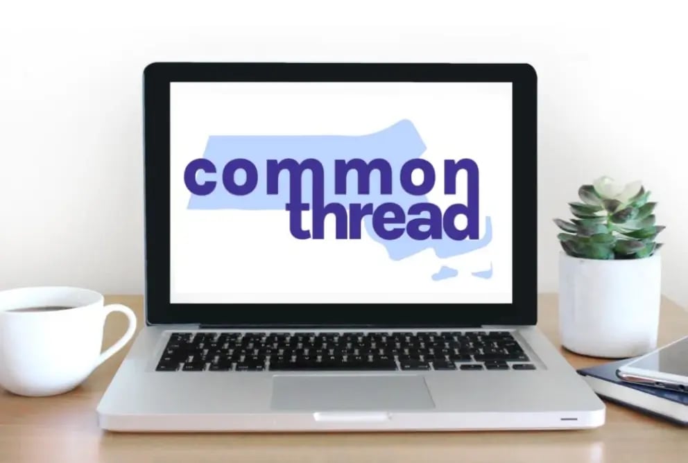 A laptop on a wooden desk displays the logo "common thread" with a blue Massachusetts outline, beside a cup and a small plant.