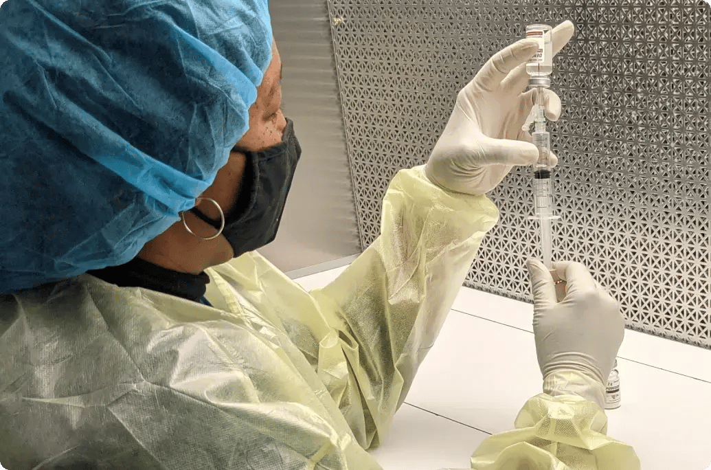 在临床环境中，一名医护人员戴着手套，穿着防护服，将疫苗从小瓶中抽入注射器，准备接种疫苗。