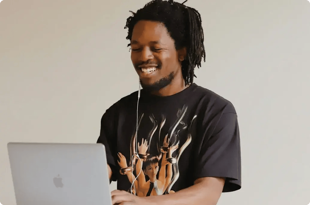 在家中使用笔记本电脑工作的人，在明亮的厨房工作区一边使用手机一边微笑。